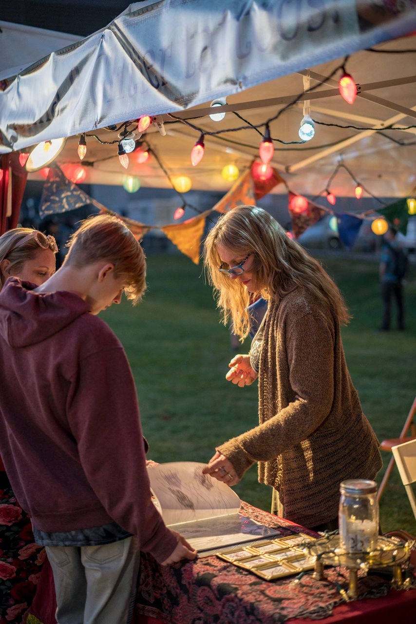 A woman stands under a tent with string lights and flips through a booklet with two other people.